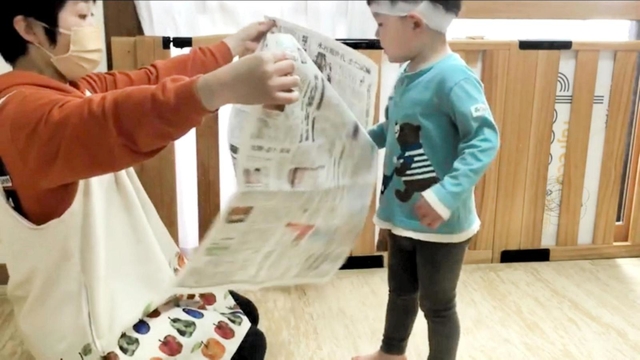 大人が広げて持った新聞紙を子どもが破く「新聞チョップ」の一場面。歩行が安定した１歳半ごろから取り組めるという