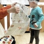 大人が広げて持った新聞紙を子どもが破く「新聞チョップ」の一場面。歩行が安定した１歳半ごろから取り組めるという