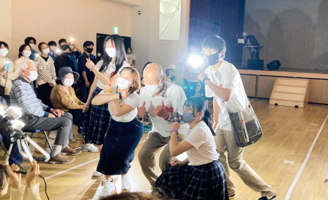 方位磁針を編み込んだブレスレットとおそろいのＴシャツでポーズを決める住民と高校生ら＝小田南生涯学習プラザ