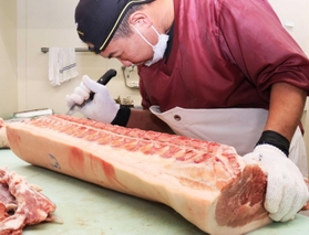 仕入れた豚肉の胴をさばく喜友名悟さん＝尼崎市玄番北之町