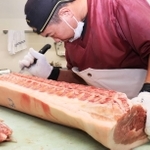 仕入れた豚肉の胴をさばく喜友名悟さん＝尼崎市玄番北之町