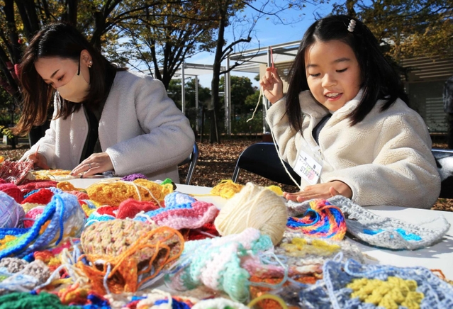 小さめの毛編みを毛糸でつなぎ合わせる親子＝芦屋市総合公園