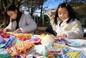 小さめの毛編みを毛糸でつなぎ合わせる親子＝芦屋市総合公園