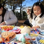 小さめの毛編みを毛糸でつなぎ合わせる親子＝芦屋市総合公園