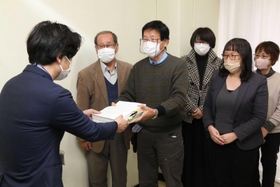 市民からの署名を市議会事務局の担当者に手渡す市民グループのメンバー＝尼崎市役所