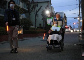 薄暗い道路を避難所スタッフが持つ誘導灯に導かれて移動する高齢夫婦＝尼崎市西昆陽１