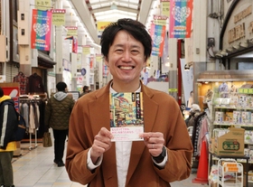 オカンとよく訪れた三和本通商店街で著書を手にほほ笑む成海隼人さん＝尼崎市神田南通２