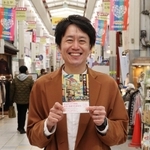 オカンとよく訪れた三和本通商店街で著書を手にほほ笑む成海隼人さん＝尼崎市神田南通２
