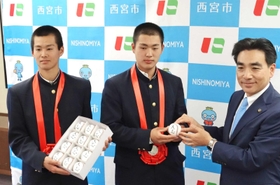 選抜高校野球大会の準優勝を報告し、石井登志郎市長（右）から「大志」と書いたボールを贈られた報徳学園の堀柊那主将（中央）と竹内颯平副主将＝西宮市役所