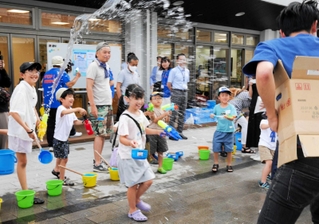 水鉄砲やひしゃくで打ち水をする参加者＝尼崎市長洲中通１