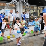 水鉄砲やひしゃくで打ち水をする参加者＝尼崎市長洲中通１