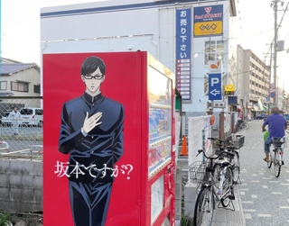 「坂本ですが？」の主人公を描いたラッピング自動販売機。奥は作品の舞台になったとされるレンタルビデオ店＝１６日夕、西宮市里中町２