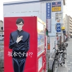 「坂本ですが？」の主人公を描いたラッピング自動販売機。奥は作品の舞台になったとされるレンタルビデオ店＝１６日夕、西宮市里中町２
