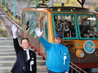 手を上げて電車の出発を合図する能勢電鉄の西中哲郎社長（左）ら＝川西市黒川