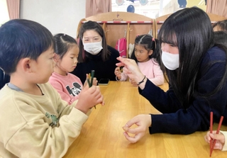 子どもたちに漆塗りの箸の使い方を教える加藤朋子さん（左から３人目）と尼崎双星高の生徒（右）＝園田愛児園