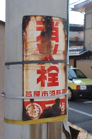 住宅街の電柱に付けられた消火栓の古びた看板。下には大手百貨店「三越」のマークと文字もある＝芦屋市大原町