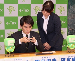 芦屋税務署の職員（右）の説明を受けながらスマートフォンで確定申告の模擬体験をする高島崚輔芦屋市長＝芦屋市役所