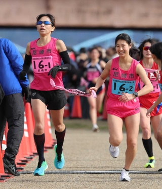 女子・尼崎市の１区志水麻紗選手（左）からたすきを受ける２区安田瑠捺選手＝加古川市の加古川河川敷マラソンコース（撮影・笠原次郎）