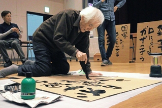 「ナクバ川柳」の墨書パフォーマンスをする木割大雄さん＝尼崎市長洲中通１、尼崎市立小田南生涯学習プラザ