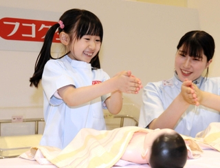 赤ちゃんをマッサージする前に手を温める子ども＝西宮市甲子園八番町、キッザニア甲子園