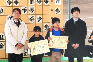 小学生将棋甲子園で優勝し、羽生善治九段（左端）、藤井聡太七冠（右端）から賞状などを受け取った低学年の部の宮野智輝さん（中央左）と澤田龍平さん＝西宮市の阪神甲子園球場（撮影・吉田敦史）