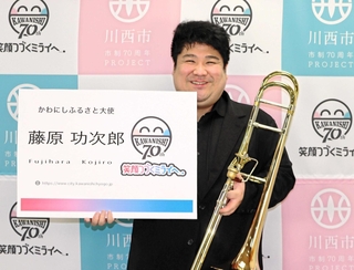 かわにしふるさと大使専用の大きな名刺を受け取りほほ笑む藤原功次郎さん＝川西市役所