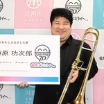 かわにしふるさと大使専用の大きな名刺を受け取りほほ笑む藤原功次郎さん＝川西市役所