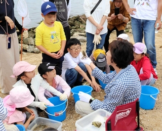 「浜・川・山の自然たんけん隊」副代表の大谷洋子さん（右手前）から、見つけたカニの話を聞く参加者＝西宮市西波止町