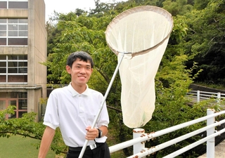 山がすぐそばまで迫る学校敷地内で網を手にする木下翔太郎さん＝西宮市鷲林寺