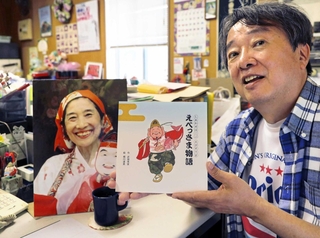 武地秀実さんが病床で書き上げた絵本「えべっさま物語」を持つ松田恵司さん。事務所の武地さんの机は亡くなる前のままで、毎日コーヒーを入れる＝西宮市田中町