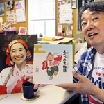 武地秀実さんが病床で書き上げた絵本「えべっさま物語」を持つ松田恵司さん。事務所の武地さんの机は亡くなる前のままで、毎日コーヒーを入れる＝西宮市田中町