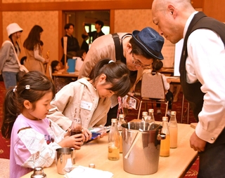 バーテンダーの助言を受けてカクテルジュース作りに取り組む子どもら＝西宮市社家町