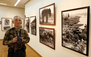 ５０回目で最後となる写壇「ゼロ」の写真展を開いた内山博司さん。手前の写真は１９７０年の万博で来日したゾウが武庫川で休む様子＝西宮市立北口ギャラリー