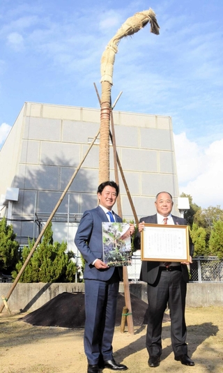橘公園に植樹されたサバルヤシを前に、松本真市長（左）から贈られた感謝状を持つ武井彰社長＝尼崎市東七松町１
