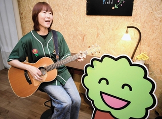 商店会「甲子園けやき散歩道」の公式テーマソングを手がけた高田志麻さん。隣にいるのは同会のキャラクター「けやきくん」＝西宮市鳴尾町１