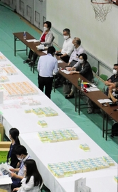 右端に並んで座るのが立会人。ここのチェックも終えた票の束が、左の白い机「集積台」に並べられていく＝１１日未明、神戸市東灘区甲南町５