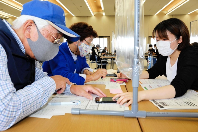 高齢者向けのワクチン接種で、姫路市役所では７日も若者による「予約お助け隊」の活動があった。２日目のこの日は大学生が中心となり、スマートフォンの苦手なお年寄りをサポート。集団接種を受けることになった夫妻は「やっと予約が取れた」と笑顔を見せた。次回の予定は未定＝姫路市安田４