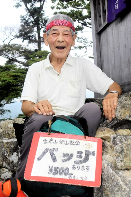 大天井岳山頂で一息つく植田将志さん。手製の看板に赤いバンダナがトレードマークだ＝姫路市夢前町山之内