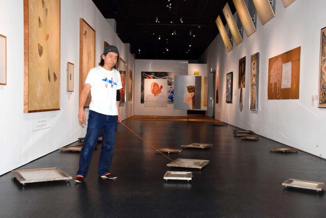 アレシンスキーと自身の作品が並ぶ会場で額縁にリードを付けて絵を移動させる日比野克彦さん＝姫路市立美術館
