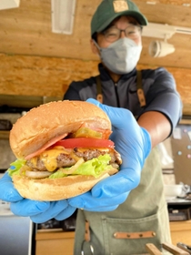 人気のベーコンチーズバーガー（７５０円）をアピールする光明寿さん＝姫路市飾東町山崎