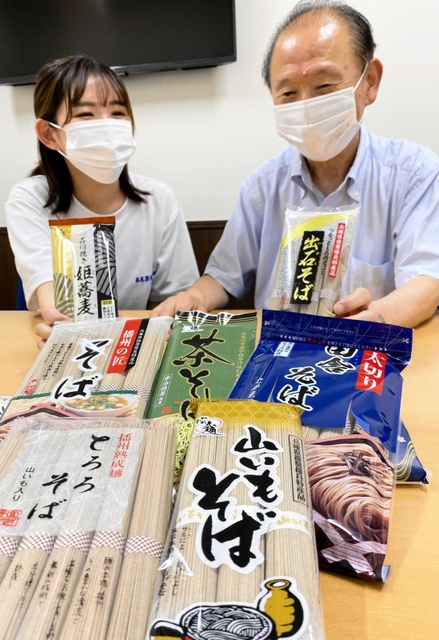 豊富なそば商品をそろえ、国内外で販売拡大を目指す高尾政秀社長（右）ら＝姫路市打越