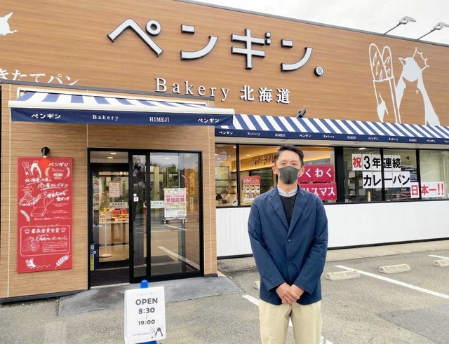ペンギンベーカリー姫路野里店前に立つ牧野光樹専務。４店目は「よい物件があれば」＝姫路市野里