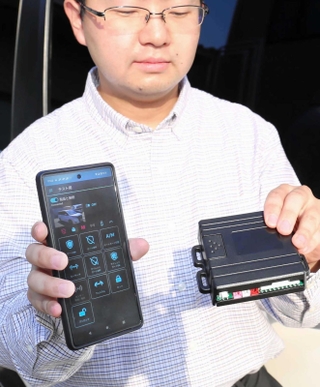 スマホと連動した車両盗難防止装置「スマートガード」を持つ服部喜優さん＝コアテックシステム