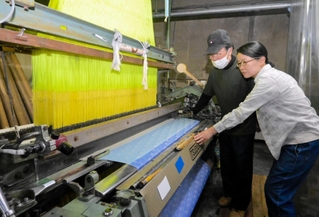 再稼働したジャカードカラミ織り機を見つめる大塚美智代さん（右）と藤原博明社長＝西脇市中畑町