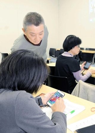 参加者にスマホの読み上げ機能を教える栗川隆宏さん（左奥）＝姫路市総合福祉会館