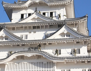 大天守の屋根に乗り、ほうきで丁寧に汚れを落とす自衛隊員＝姫路市本町
