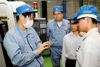 金属部品を手に、新興精機製作所の作業員（左）から技を学ぶ飾磨工業高校の生徒ら＝姫路市阿保