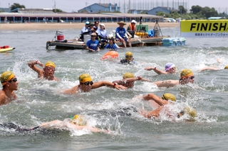 水しぶきを上げ、勢いよく泳ぎ出す参加者たち＝姫路市的形町、的形海水浴場沖