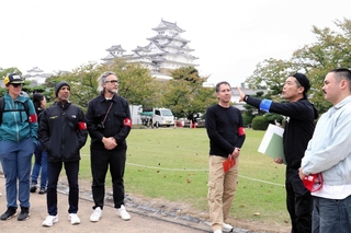 姫路フィルムコミッションの井上正也部長（右から２人目）から姫路城の解説を聞くハリウッド関係者＝姫路市本町