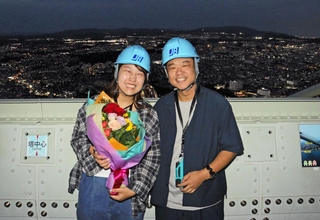 高さ約３００メートルから望む夜景をバックにプロポーズした本久仁彦さん。お相手の堀江由香さんと記念写真に納まった＝明石海峡大橋